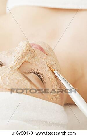 Stock Image - Close up of woman's face with beauty mask being applied, Studio shot. Fotosearch