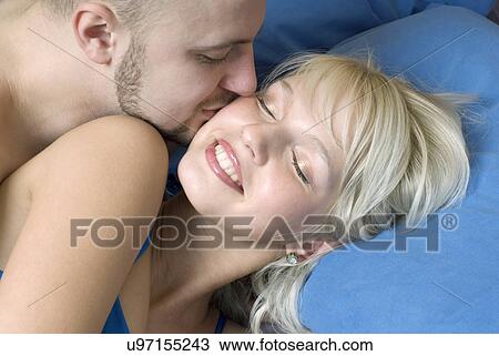 Stock Image - Close-up of young man kissing woman in bed. Fotosearch