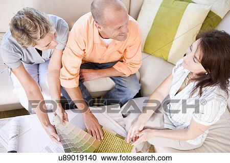 Stock Image - Couple and interior designer sitting on sofa and choosing color sample, high angle view. Fotosearch