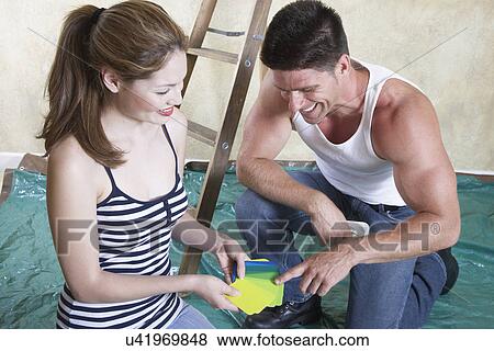Stock Photo - Couple looking at color samples in drop cloth covered room. Fotosearch