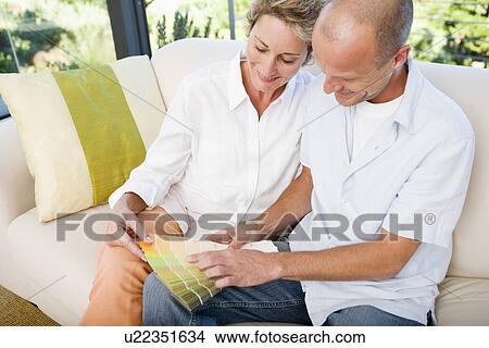 Picture - Couple on sofa looking at color samples, smiling. Fotosearch