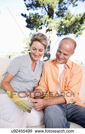 Stock Photo - Couple on sofa looking at color samples, smiling. Fotosearch