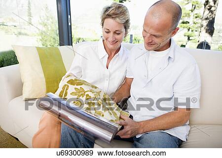Stock Photo - Couple on sofa looking at fabric swatches, smiling. Fotosearch