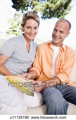 Stock Image - Couple on sofa looking holding color samples, smiling, portrait. Fotosearch