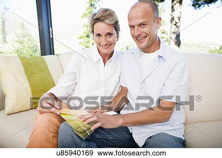 Stock Photo - Couple on sofa looking holding color samples, smiling, portrait. Fotosearch