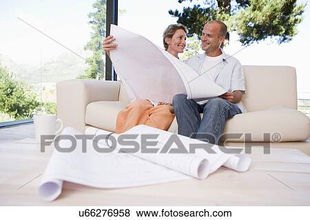 Stock Photo - Couple sitting on sofa with blueprints in foreground. Fotosearch