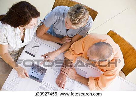 Stock Photograph - Couple with female architect looking at blueprint, high angle view. Fotosearch