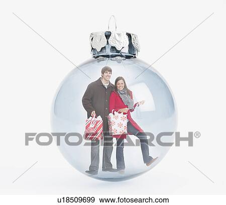 Stock Photo - Digital composite of smiling people with shopping bags inside christmas bulb. Fotosearch