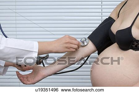 Stock Photograph - Doctor taking pregnant woman's blood pressure, mid section. Fotosearch