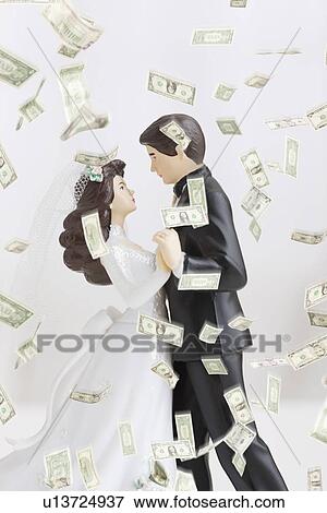 Stock Photo - Dollar banknotes falling on bride and groom figurines. Fotosearch
