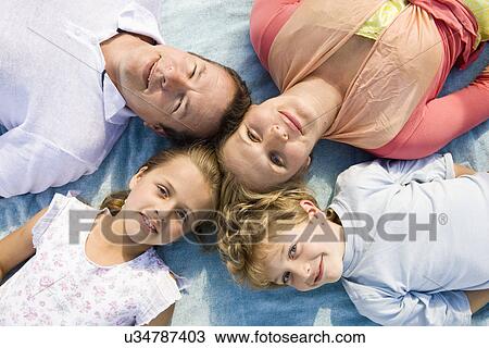 Stock Image - Family including boy and girl (8-9) lying on blanket, portrait. Fotosearch