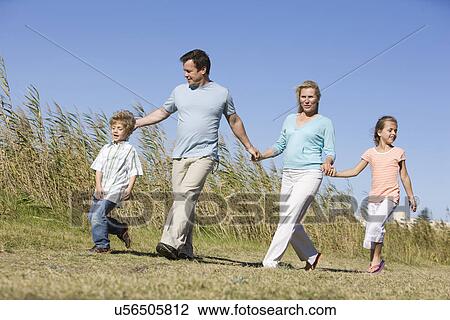 Stock Image - Family including boy and girl (8-9) walking in field. Fotosearch