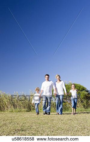 Stock Photo - Family including boy and girl (8-9) walking across grassy field. Fotosearch
