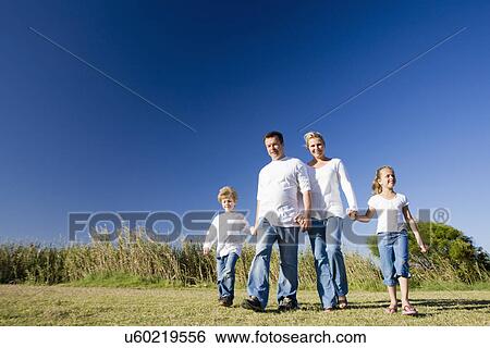 Stock Photograph - Family including boy and girl (8-9) walking across grassy field. Fotosearch
