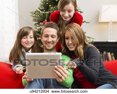 Family with two children (8-9, 10-11) using laptop sitting ahead of Christmas tree View Large Photo Image Picture - Family with two children (8-9, 10-11) using laptop sitting ahead of Christmas tree. Fotosearch