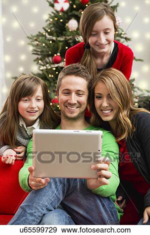 Stock Photo - Family with two children (8-9, 10-11) using laptop sitting ahead of Christmas tree. Fotosearch