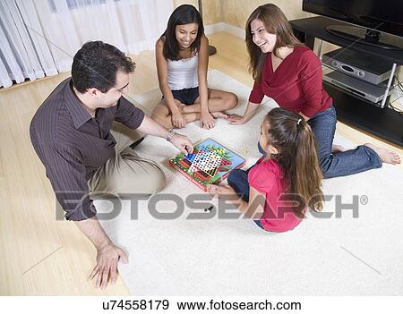 Stock Photo - Family with two girls (8-9, 12-13) playing chinese checkers in living room. Fotosearch