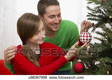 Stock Photo - Father and daughter (10-11) decorating Christmas tree. Fotosearch