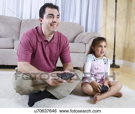Stock Photograph - Father and daughter (6-7) playing video game. Fotosearch