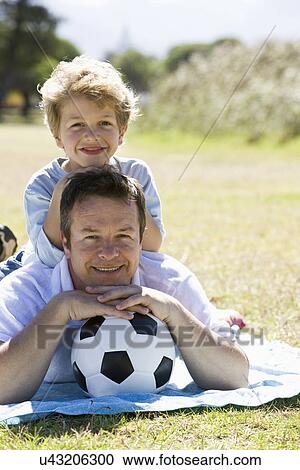 Stock Image - Father and son (8-9) laying on lawn, portrait. Fotosearch