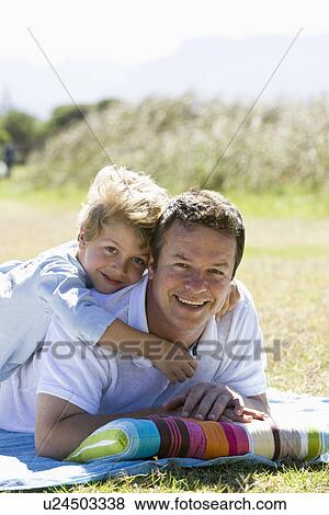 Stock Photo - Father and son (8-9) laying on lawn, portrait. Fotosearch