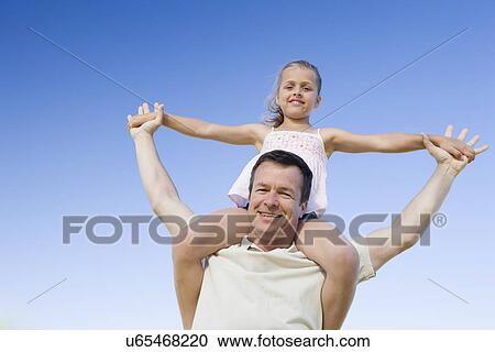 Stock Image - Father carrying daughter (8-9) on shoulders, portrait. Fotosearch