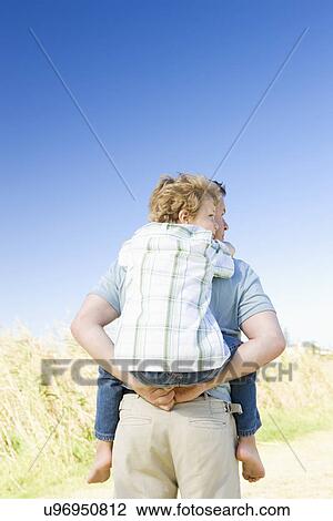 Stock Image - Father carrying son (8-9) on shoulders, rear view. Fotosearch