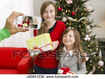 Stock Photo - Father photographing his two daughters (8-9, 10-11) with Christmas gifts. Fotosearch