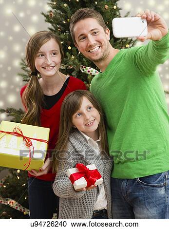 Father with two daughters (8-9, 10-11) photographing themselves with Christmas gifts View Large Photo Image Stock Image - Father with two daughters (8-9, 10-11) photographing themselves with Christmas gifts. Fotosearch