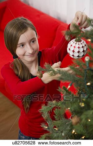 Stock Photo - Girl (10-11) decorating Christmas tree. Fotosearch