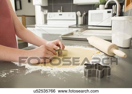 Stock Photograph - Girl (12-13) cutting cookie. Fotosearch