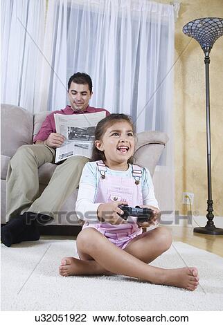 Girl (6-7) playing video game, father reading newspaper in background View Large Photo Image Stock Image - Girl (6-7) playing video game, father reading newspaper in background. Fotosearch
