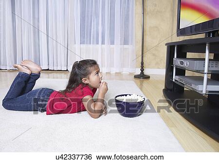 Stock Photograph - Girl (6-7) watching television and eating pop corn. Fotosearch