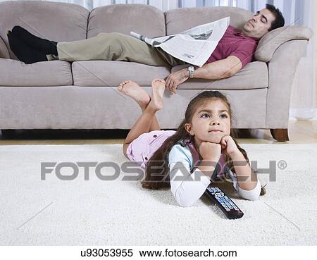 Girl (6-7) watching television, father with newspaper sleeping on sofa in background View Large Photo Image Stock Photography - Girl (6-7) watching television, father with newspaper sleeping on sofa in background. Fotosearch