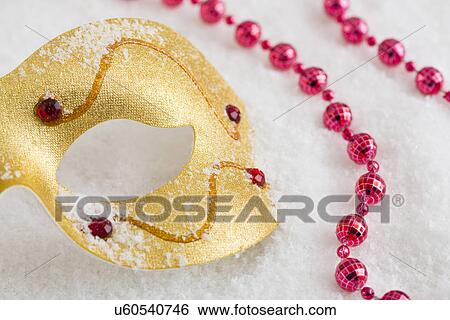 Stock Photograph - Golden mask and red necklace on snow. Fotosearch