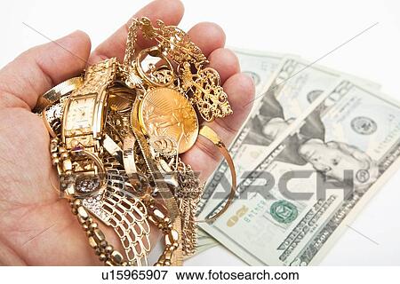 Stock Photo - Hand holding gold jewelry, banknotes in background. Fotosearch