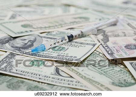 Stock Image - High angle view of syringe on US banknotes, studio shot. Fotosearch