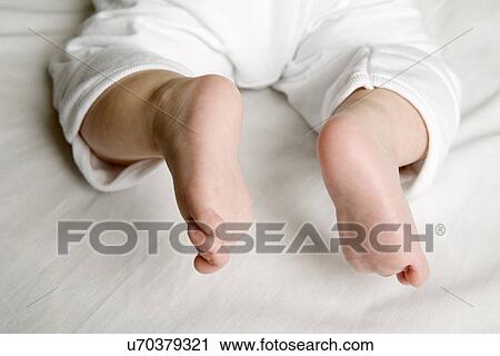 Stock Image - Low section of baby (2-5 months) lying on front on bed. Fotosearch