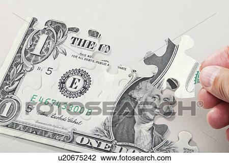 Stock Image - Male hand arranging puzzle pieces creating dollar bill. Fotosearch
