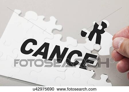 Stock Image - Male hand arranging puzzle pieces spelling out CANCER. Fotosearch