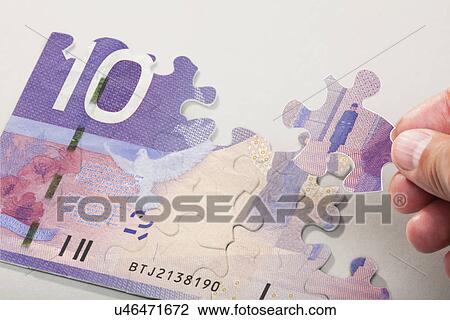 Stock Image - Male hand arranging puzzle pieces creating canadian currency. Fotosearch