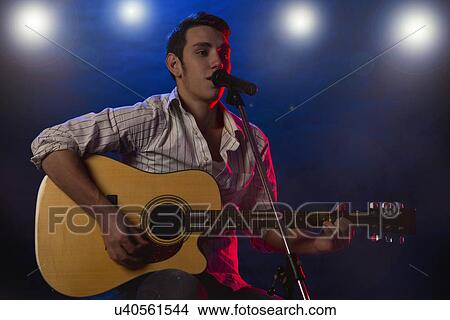 Picture - Male musician playing guitar and singing on stage. Fotosearch