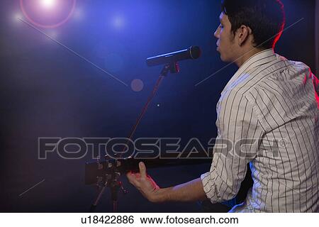 Male musician playing guitar and singing on stage View Large Photo Image Stock Photograph - Male musician playing guitar and singing on stage. Fotosearch