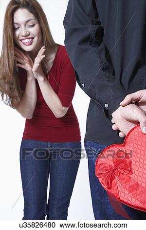 Man hiding Valentine's gift in front of woman View Large Photo Image Stock Image - Man hiding Valentine's gift in front of woman. Fotosearch