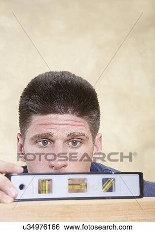 Man looking at level on piece of wood View Large Photo Image Stock Photograph - Man looking at level on piece of wood. Fotosearch
