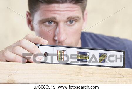 Stock Photography - Man looking at level on piece of wood. Fotosearch