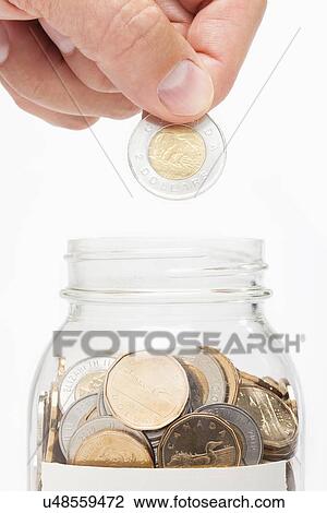Stock Image - Man putting coin into jar. Fotosearch