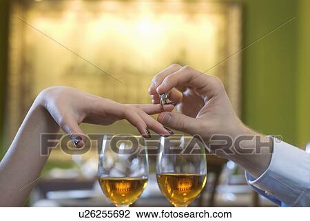 Man putting engagement ring on woman's finger above white wine glasses, close-up of hands View Large Photo Image Stock Image - Man putting engagement ring on woman's finger above white wine glasses, close-up of hands. Fotosearch