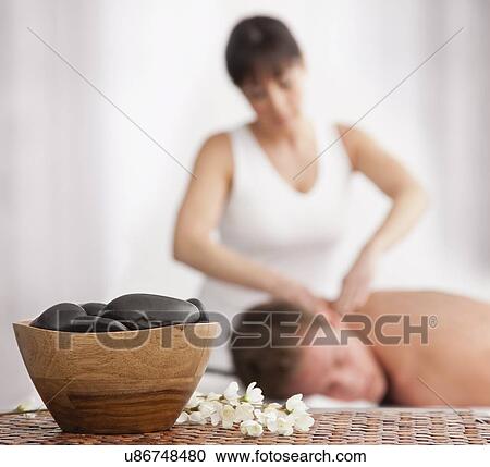 Stock Image - Man receiving massage, stones in bowl in foreground. Fotosearch