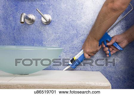 Stock Image - Man using caulking gun, close-up. Fotosearch
